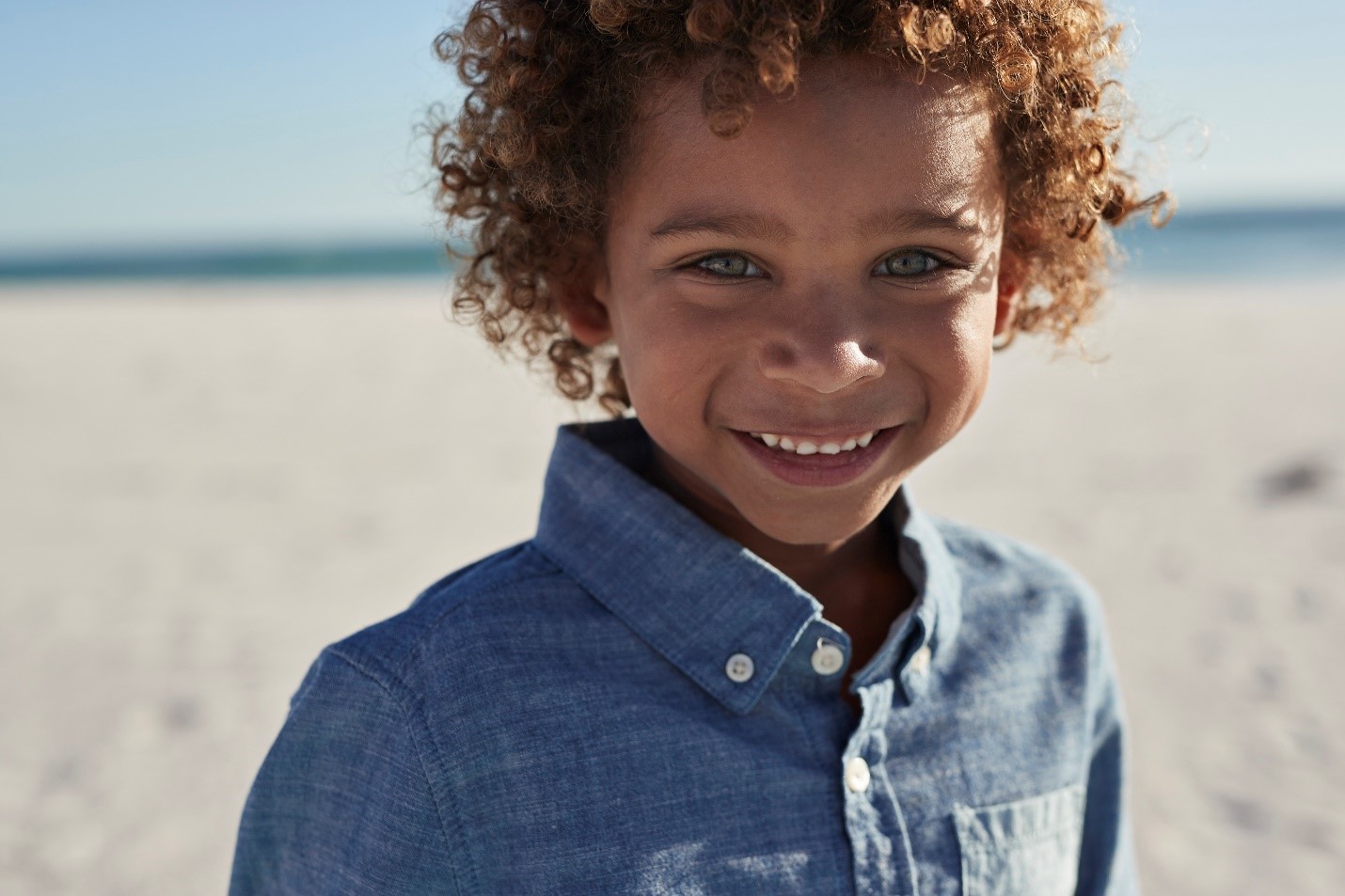 Child Care and Development Contacts photo tile with young boy on a beach smiling. 